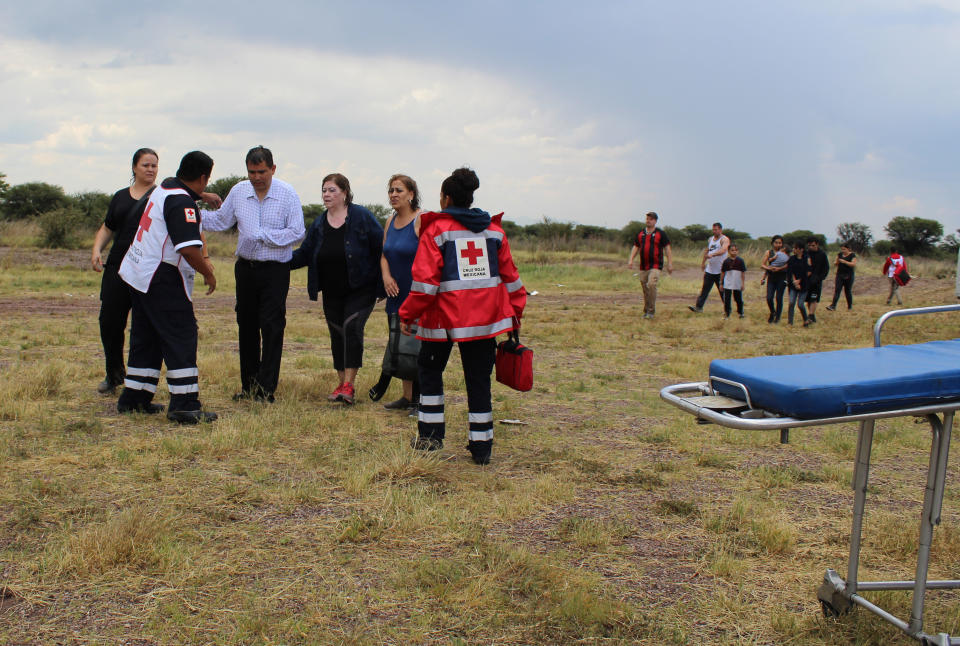 In this photo released by Red Cross Durango communications office, Red Cross workers attend airline passengers who survived a plane crash, as they walk away from the crash site in a field near the airport in Durango, Mexico, Tuesday, July 31, 2018. An Aeromexico jetliner crashed while taking off during a severe storm, smacking down in a field nearly intact then catching fire, and officials said it appeared everyone on board escaped the flames. (Red Cross Durango via AP)