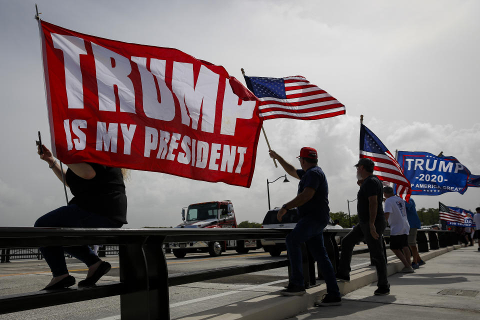 Trump supporters hold flags saying: Trump Is My President and Trump 2020.