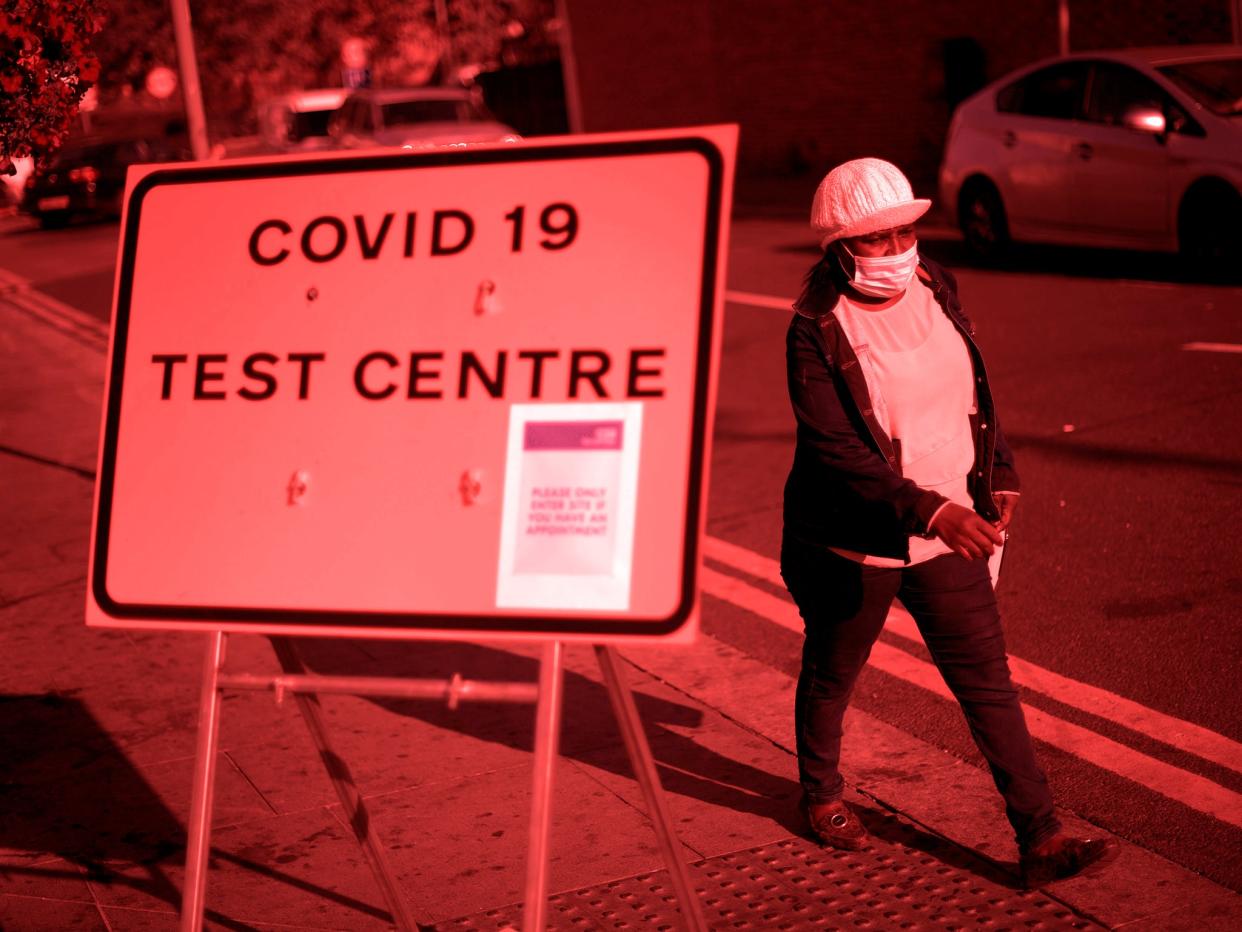 Pedestrian wearing facemask walks past a sign for a Covid-19 test centre in Leyton, east London on 19 September (AFP via Getty)