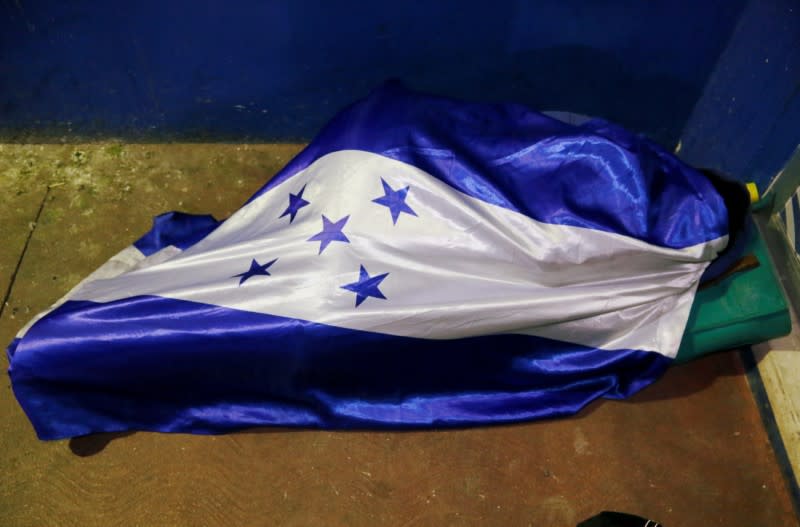 A person, part of a caravan of migrants heading toward the United States, rests covered in a Honduras' national flag, at the border between Honduras and Guatemala in Agua Caliente