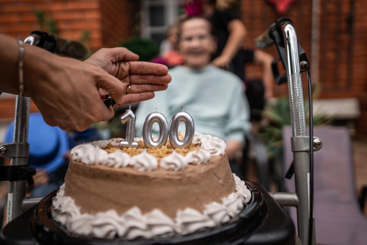 Someone lighting candles shaped like the number 100, in front of an older lady.