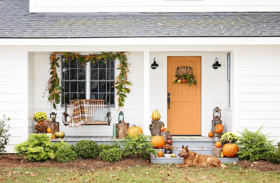 white exterior with orange front door and stairs covered in wood stumps and pumpkins