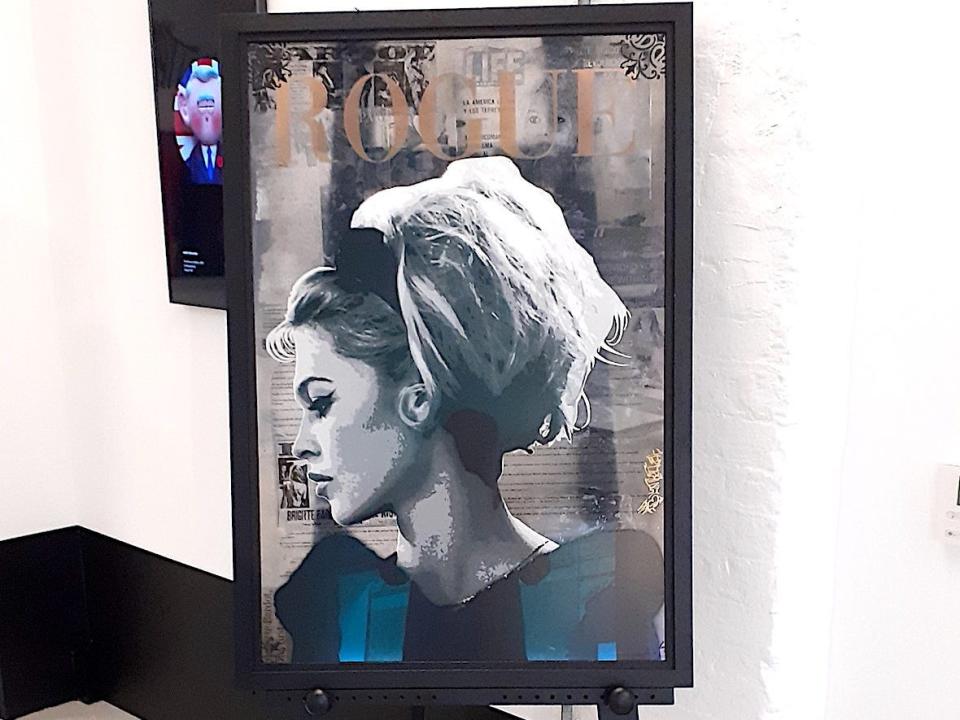 A picture by the artists Bluntroller is displayed on an easel. It features a women. The words Rouge are written across the top, in imitation of a Vogue magazine cover.