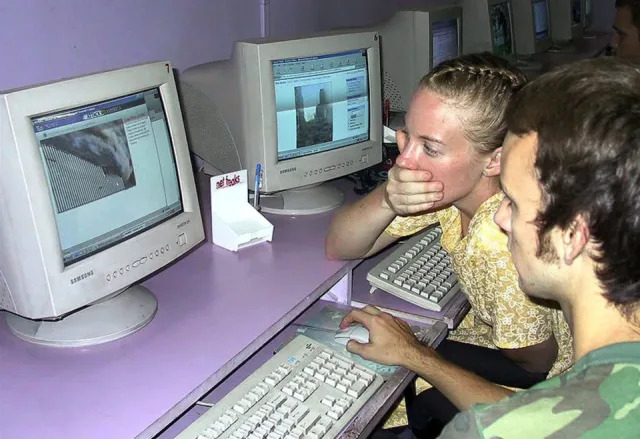 Los turistas estadounidenses Ted Barnett (en el centro) y Jamie Otten mirando las fotos de los ataques a los edificios del World Trade Center en un cibercafé en Calcuta, el 12 de septiembre de 2001. Tres aviones requisados por secuestradores se estrellaron contra el Pentágono y las torres gemelas del World Trade Center.