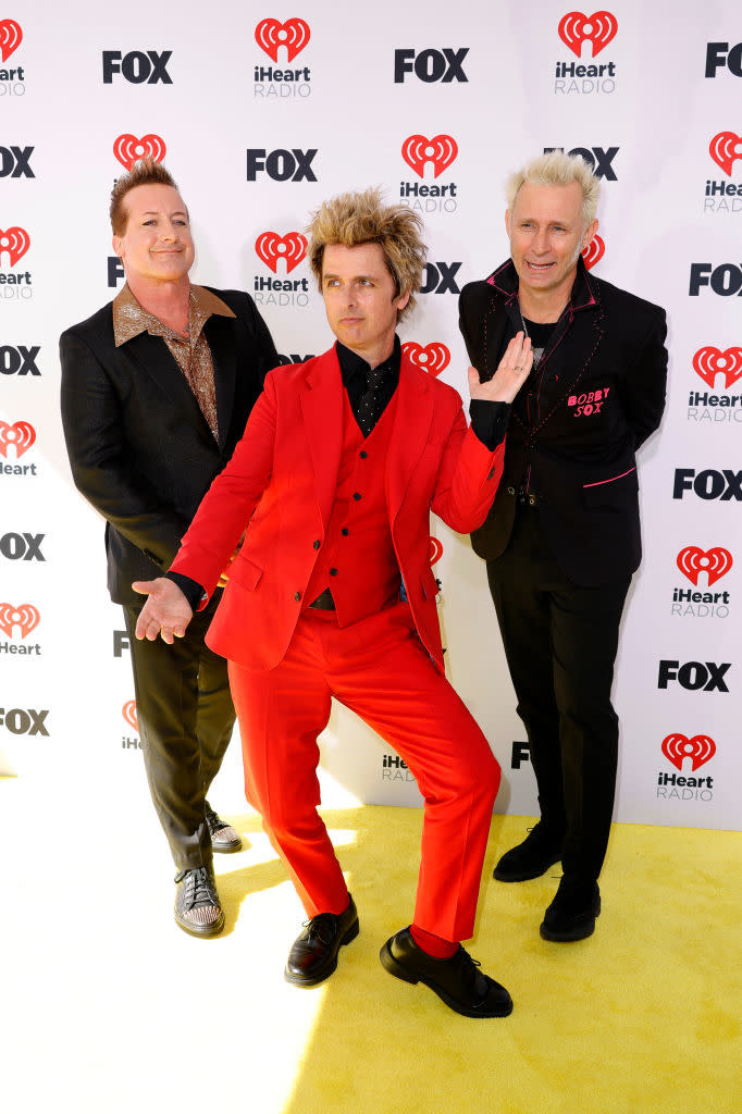 Tre Cool, Billie Joe Armstrong, and Mike Dirnt of Green Day pose at an event, Armstrong in a distinctive red suit