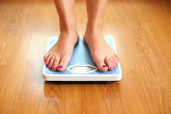 Female bare feet with weight scale on wooden floor