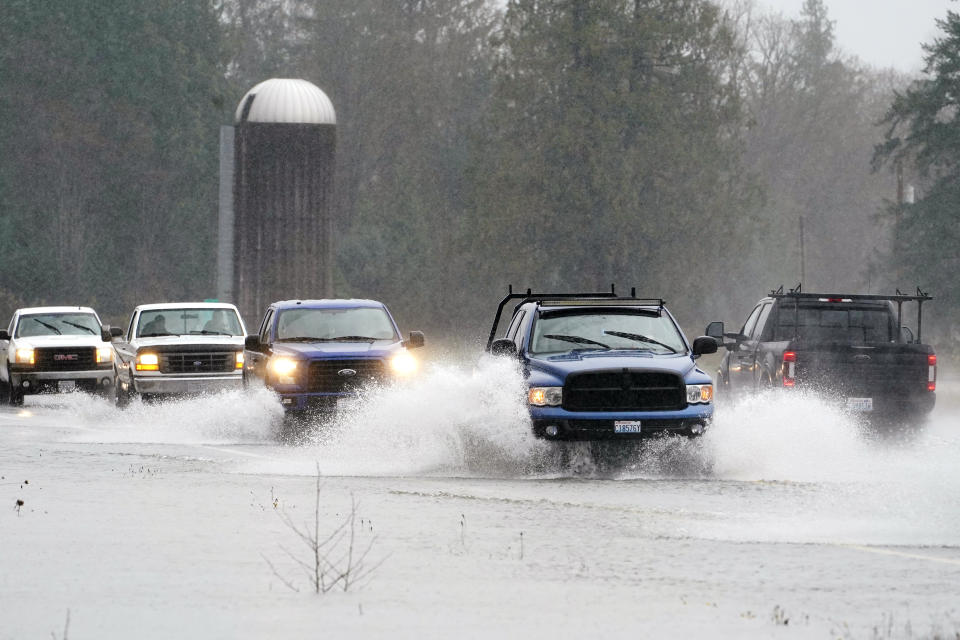 Traffic continues through water over the roadway on Highway 20, Monday, Nov. 15, 2021, near Hamilton, Wash. The heavy rainfall of recent days brought major flooding of the Skagit River that is expected to continue into at least Monday evening. (AP Photo/Elaine Thompson)
