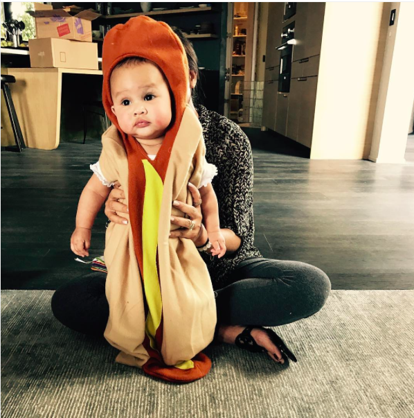 Chrissy Teigen holds up her baby girl, Luna, dressed as a hot dog.