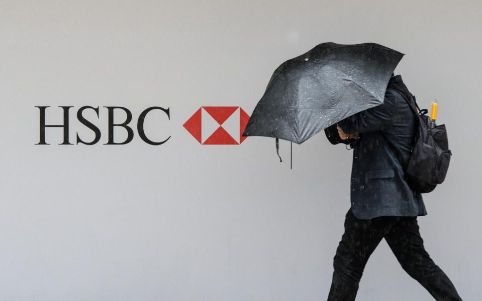 A person with an umbrella walks past an HSBC sign