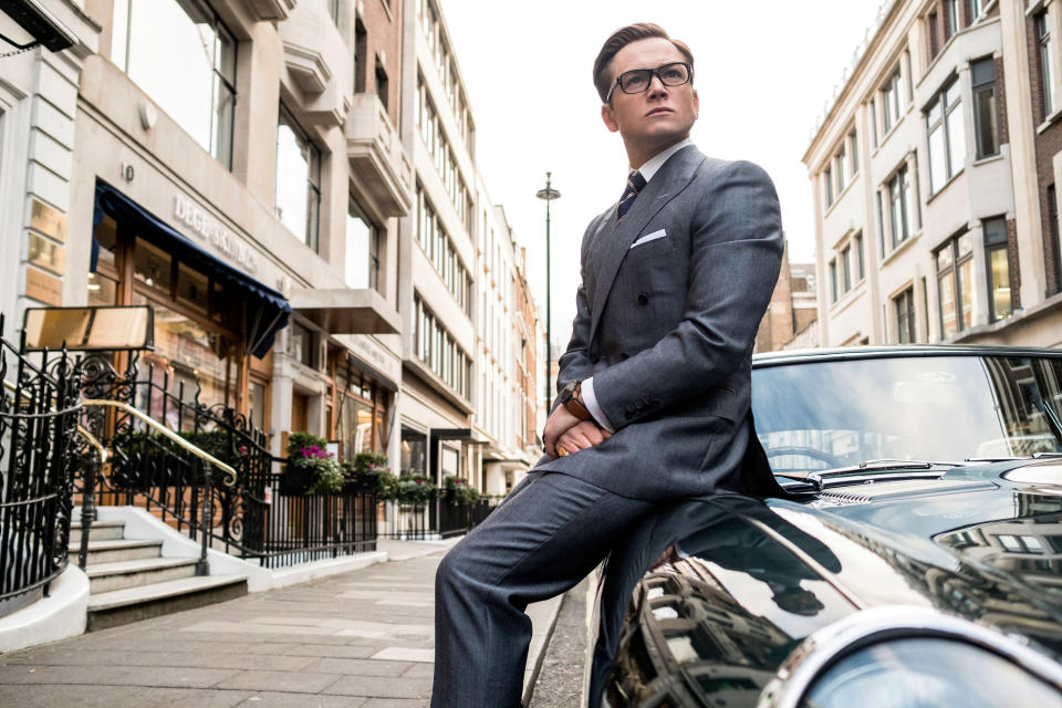 Taron Egerton in a suit leaning on a fancy car