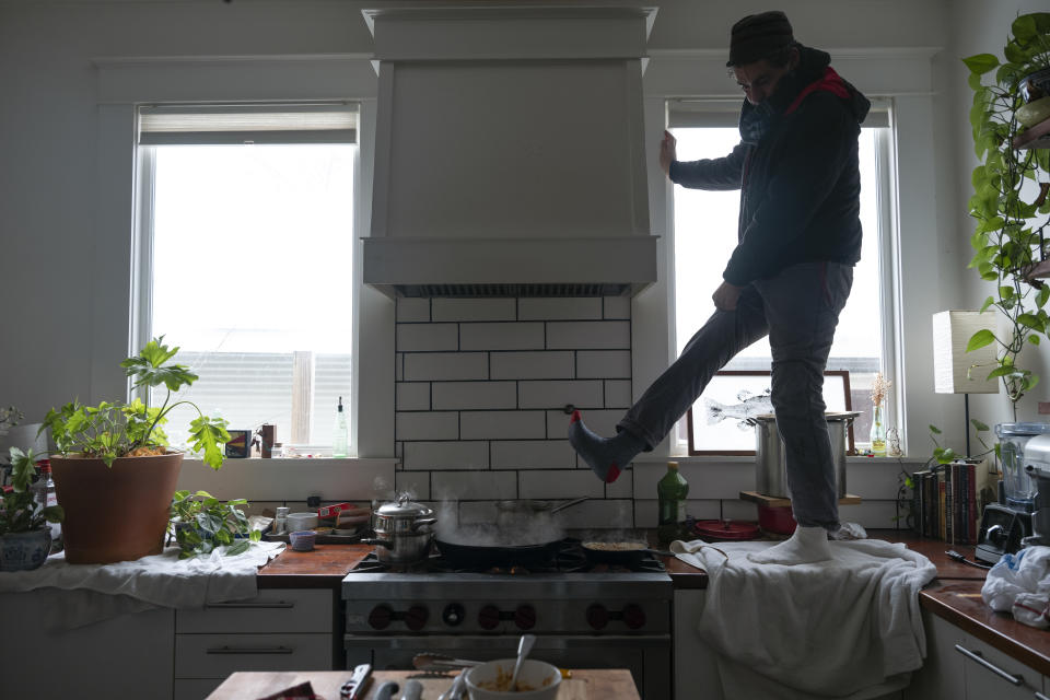 Jorge Sanhueza-Lyon stands on his kitchen counter to warm his feet over his gas stove Tuesday, Feb. 16, 2021, in Austin, Texas. Power was out for thousands of central Texas residents after temperatures dropped into the single digits when a snow storm hit the area on Sunday night. (AP Photo/Ashley Landis)