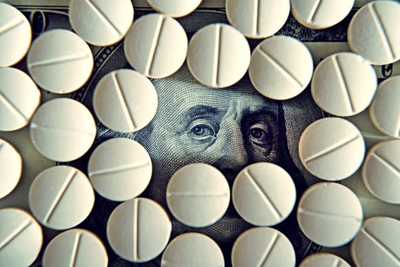 Prescription tablets lying on a hundred dollar bill, covering all of Ben Franklin's face except for his eyes.