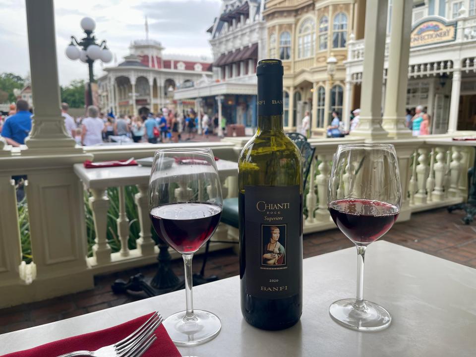 wine bottle and two glasses on a table overlooking main street usa at tony's town square restaurant in magic kingdom at disney world