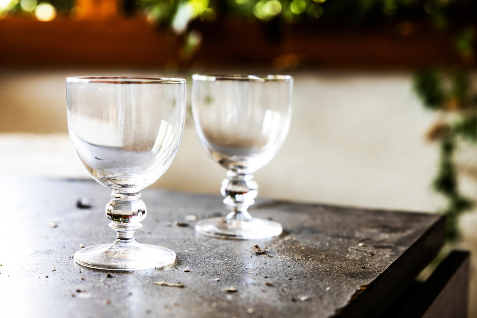 Two empty wine glasses sit on a table outdoors, surrounded by greenery