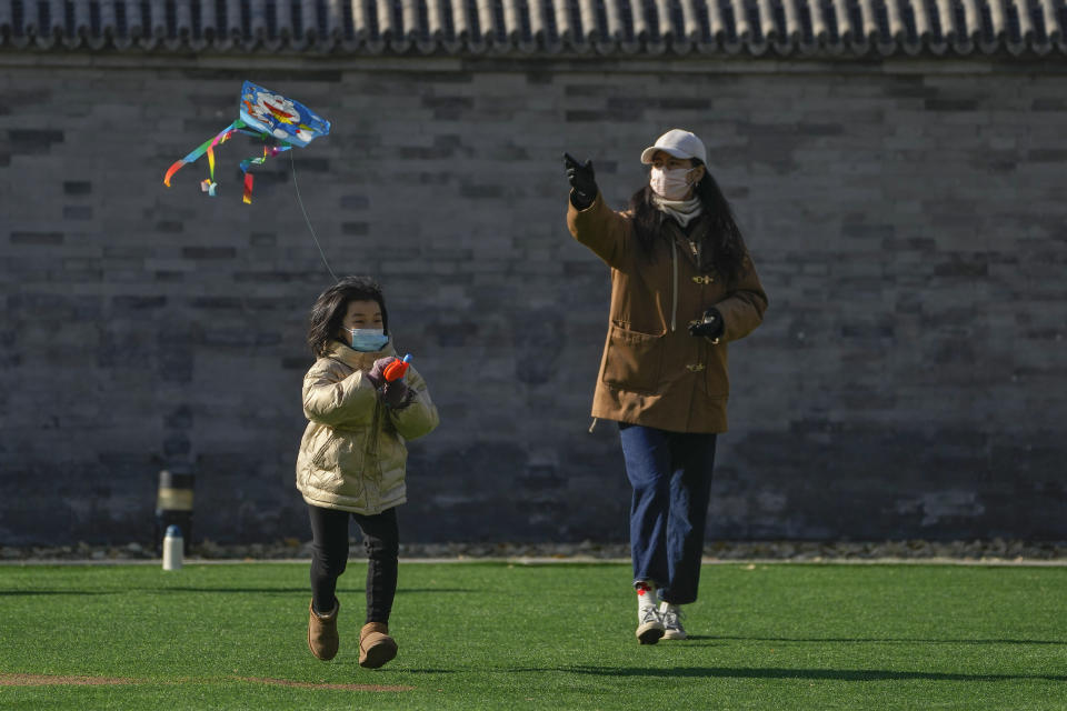 A woman and a child fly kite on a green outside a mall in Beijing, Sunday, Dec. 4, 2022. China on Sunday reported two additional deaths from COVID-19 as some cities move cautiously to ease anti-pandemic restrictions amid increasingly vocal public frustration over the measures. (AP Photo/Andy Wong)