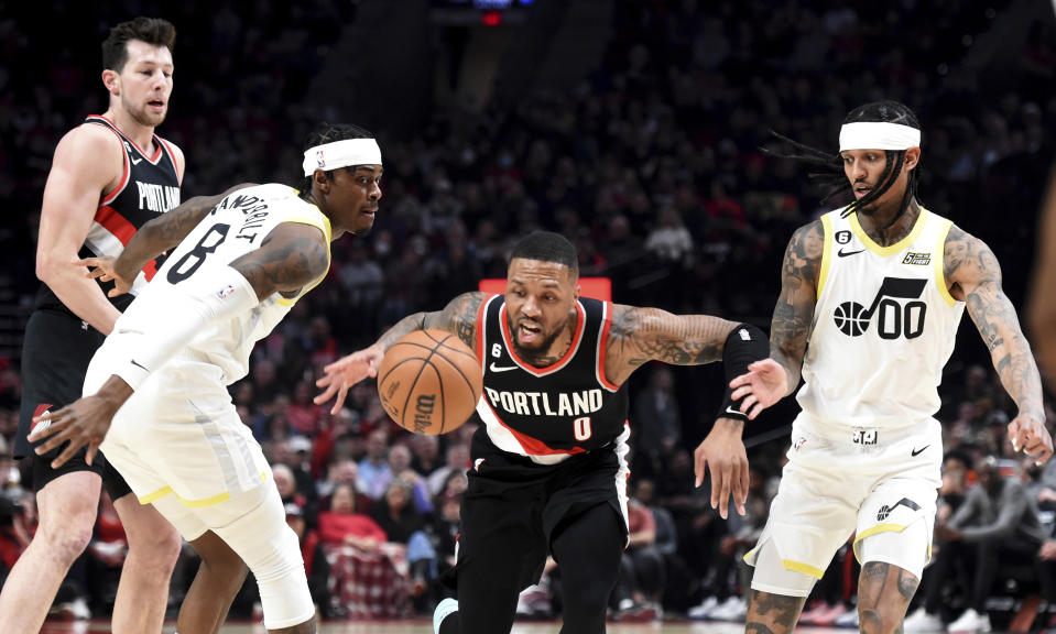 Portland Trail Blazers guard Damian Lillard, center, dribbles the ball past Utah Jazz forward Jarred Vanderbilt, left, and guard Jordan Clarkson during the first half of an NBA basketball game in Portland, Ore., Wednesday, Jan. 25, 2023. (AP Photo/Steve Dykes)