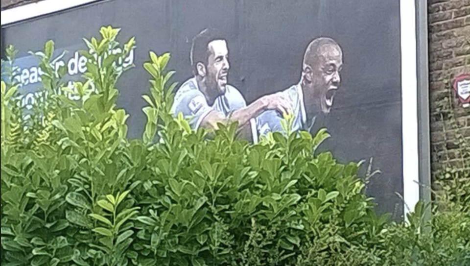 Billboard showing two excited soccer players celebrating, partially obscured by green shrubbery