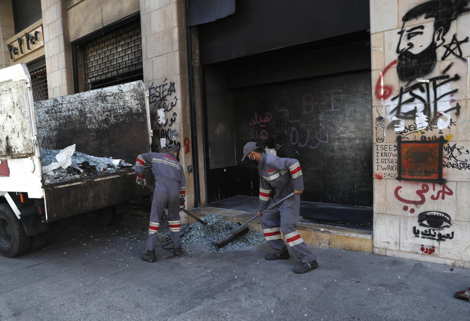 Workers remove broken glass of a window shop that was damaged by protesters during an anti-government rally in Beirut, Lebanon, Friday, June 12, 2020. Lebanon's prime minister held an emergency Cabinet meeting Friday, hours after demonstrators shut roads across the country with burning tires in renewed nationwide protests spurred by a plunging national currency and economic crisis. (AP Photo/Hussein Malla)