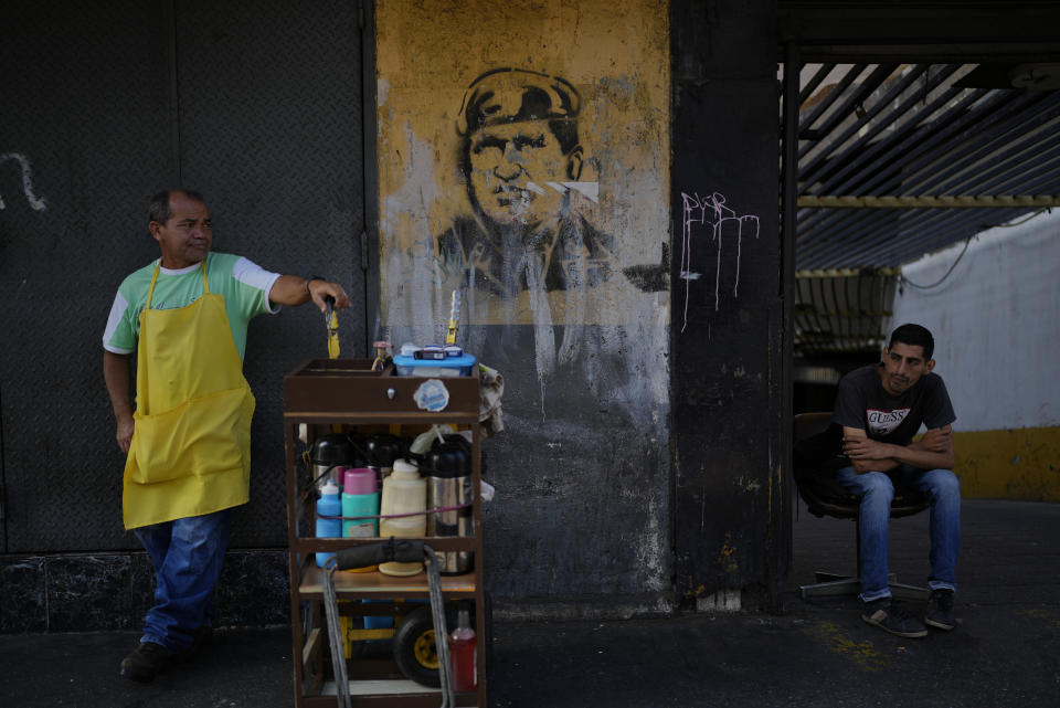 A stencil of the late Venezuelan President Hugo Chavez decorates the entrance of a parking lot where a coffee vendor waits for clients, in Caracas, Venezuela, Tuesday, Feb. 28, 2023. About three-quarters of Venezuelans live on less than $1.90 a day — the international benchmark of extreme poverty. The minimum wage paid in bolivars is the equivalent of $5 per month. (AP Photo/Ariana Cubillos)