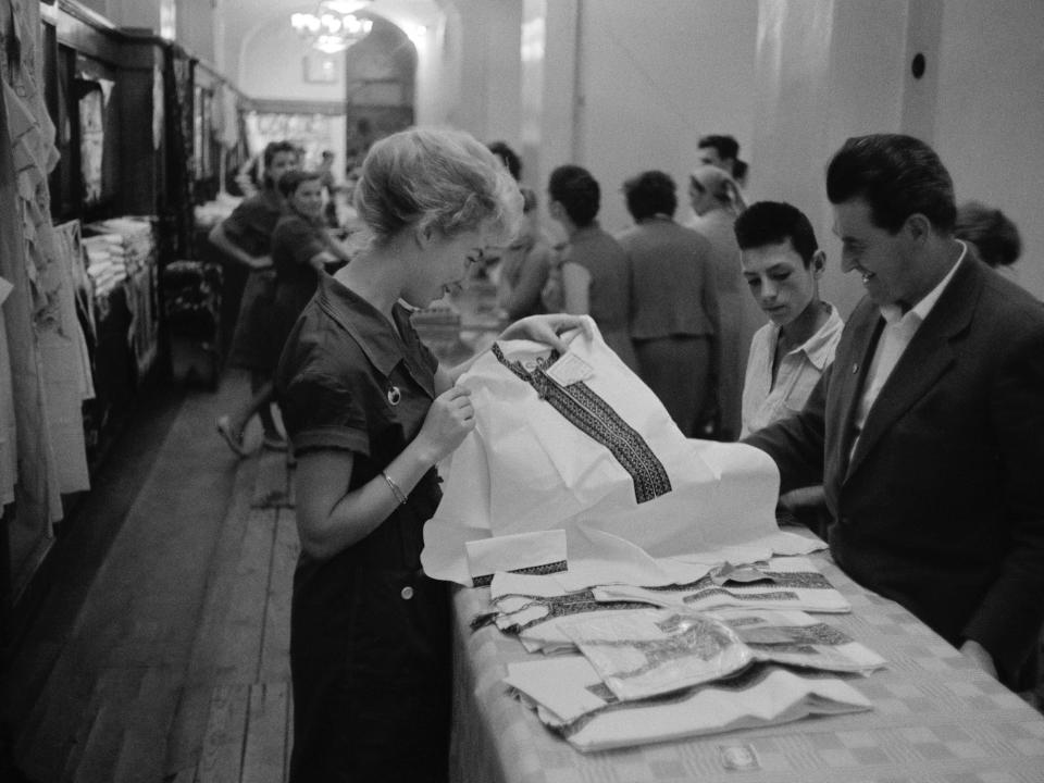 A sales assistant shows clothing to shoppers in the GUM department store, in Red Square, Moscow, Russia, Soviet Union, 1961.