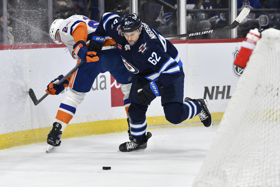 New York Islanders' Scott Mayfield (24) and Winnipeg Jets' Nino Niederreiter (62) compete for the puck behind the net during the second period of an NHL hockey game Tuesday, Jan. 16, 2024, in Winnipeg, Manitoba. (Fred Greenslade/The Canadian Press via AP)