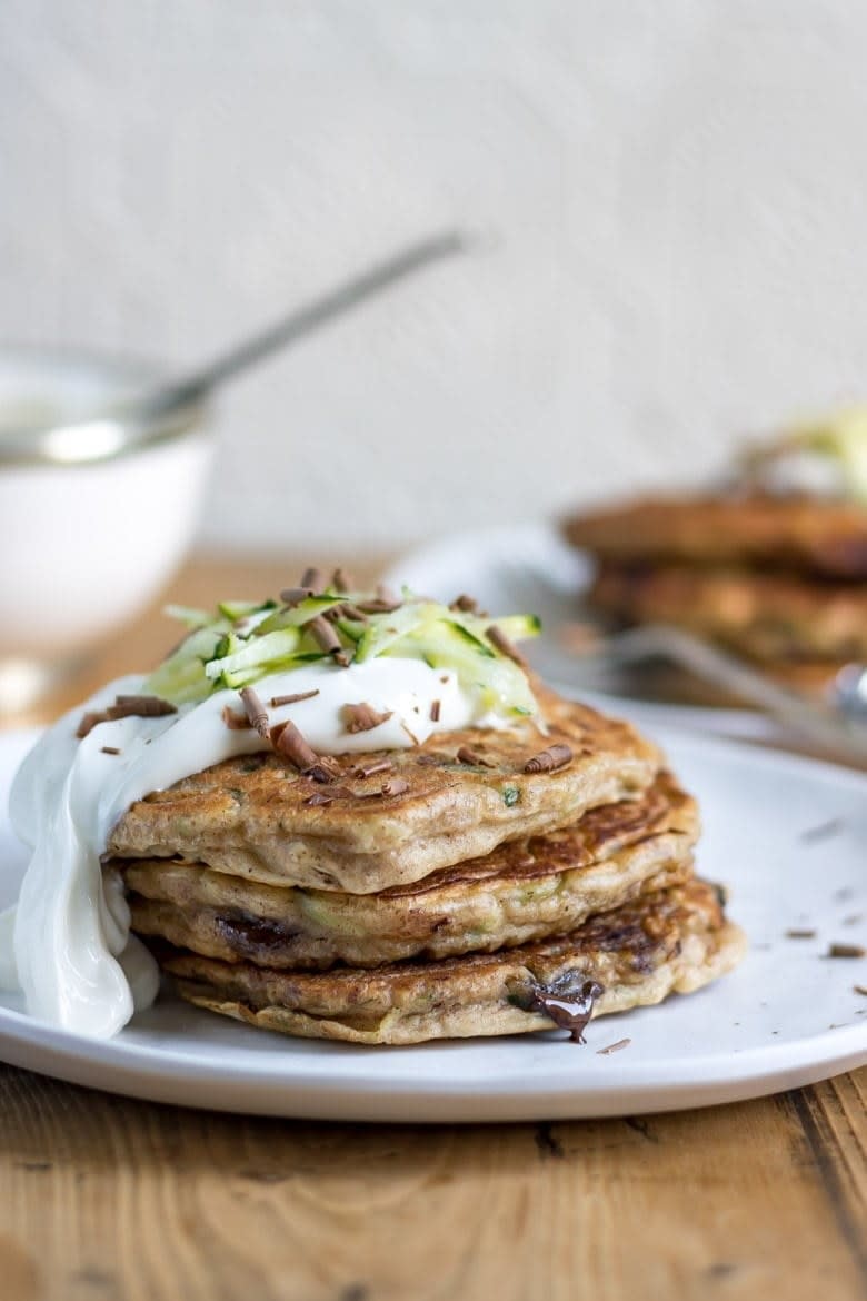 Three chocolate zucchini pancakes stacked on a plate and covered with a creamy sauce