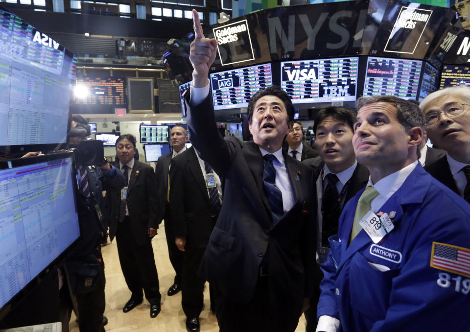 FILE - In this Wednesday, Sept. 25, 2013 file photo, Japan's Prime Minister Shinzo Abe, center, points to stock listing at the post of specialist Anthony Rinaldi, foreground right, during his tour of the trading floor before ringing the New York Stock Exchange closing bell. Abe has ticked off the easy items on his to-do list for economic revival. Flashy indicators show that factories are churning out more cars and high-definition TVs. Corporate profits are up. Stock prices gained 29 percent in the past year. Despite his brash declaration that “Japan is back” in a speech last September to the New York Stock Exchange, Abe faces a thornier challenge in ensuring that his “Abenomics” recovery spreads beyond boardrooms and investment portfolios. (AP Photo/Richard Drew, File)