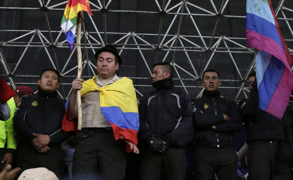 A policeman detained by anti-governments protesters is made to hold an indigenous banner while standing on a stage, in Quito, Ecuador, Thursday, Oct. 10, 2019. Thousands of protesters staged anti-government rallies Wednesday, seeking to intensify pressure on Ecuador's president after a week of unrest sparked by fuel price hikes. (AP Photo/Dolores Ochoa)