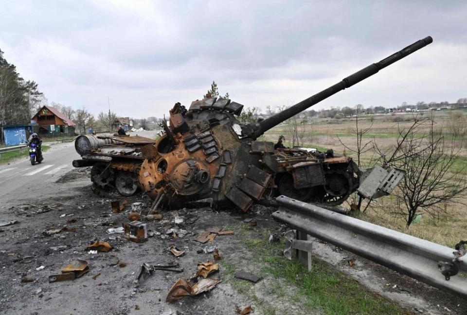 A man ride a motorbike past a destroyed Russian tank on a road in the village of Rusaniv, in the Kyiv region on April 16, 2022.