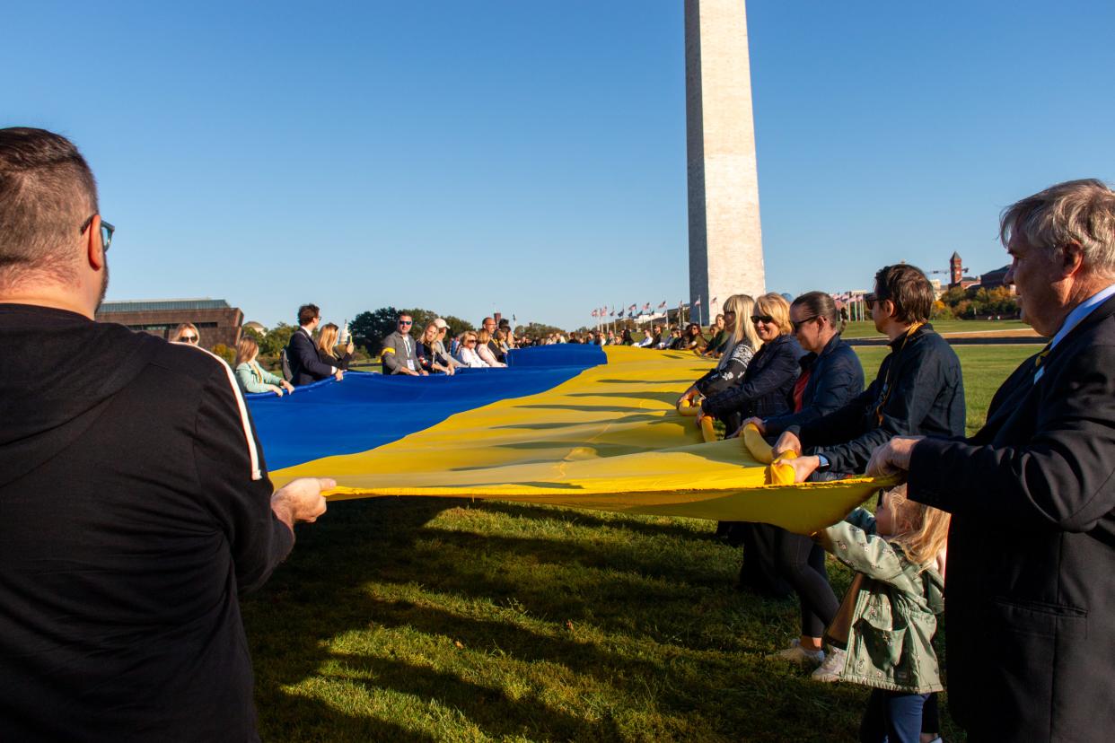 people holding blue and yellow flag, washington monument in distance