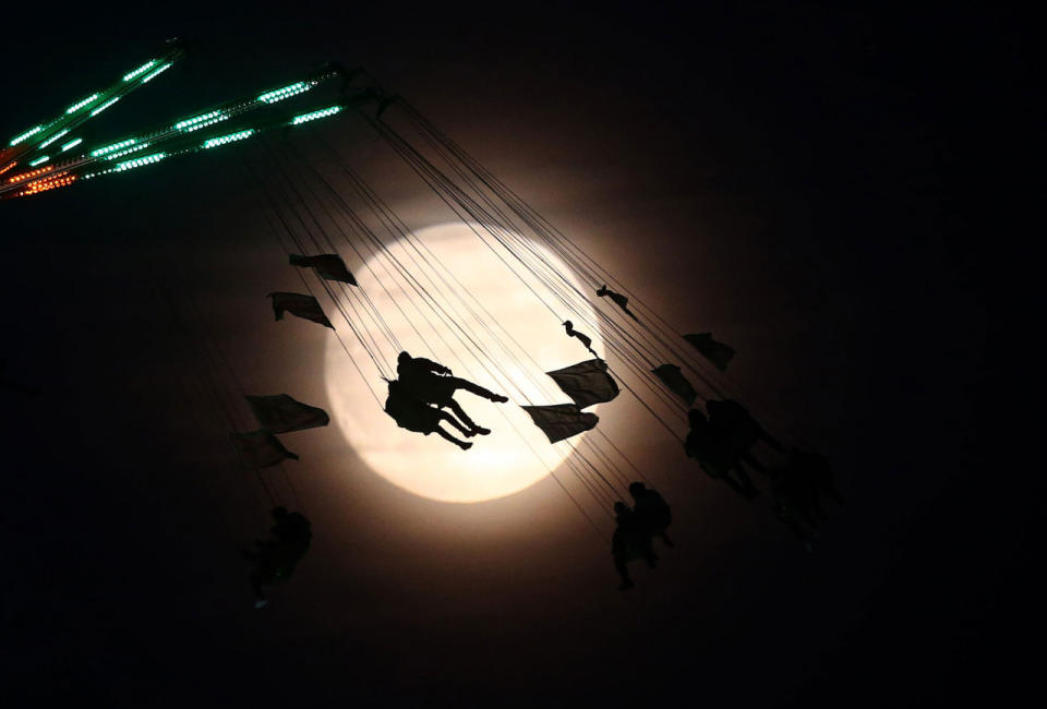 Varia gente en un paseo de la diversión queda silueteada en la luna un día antes del espectáculo de la “supermoon”, en Londres, Gran Bretaña 13 de noviembre, 2016. (REUTERS / Neil Hall)