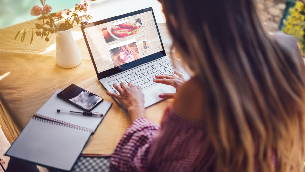 Young food blogger entrepreneur writing blog post and working online on laptop from home office.