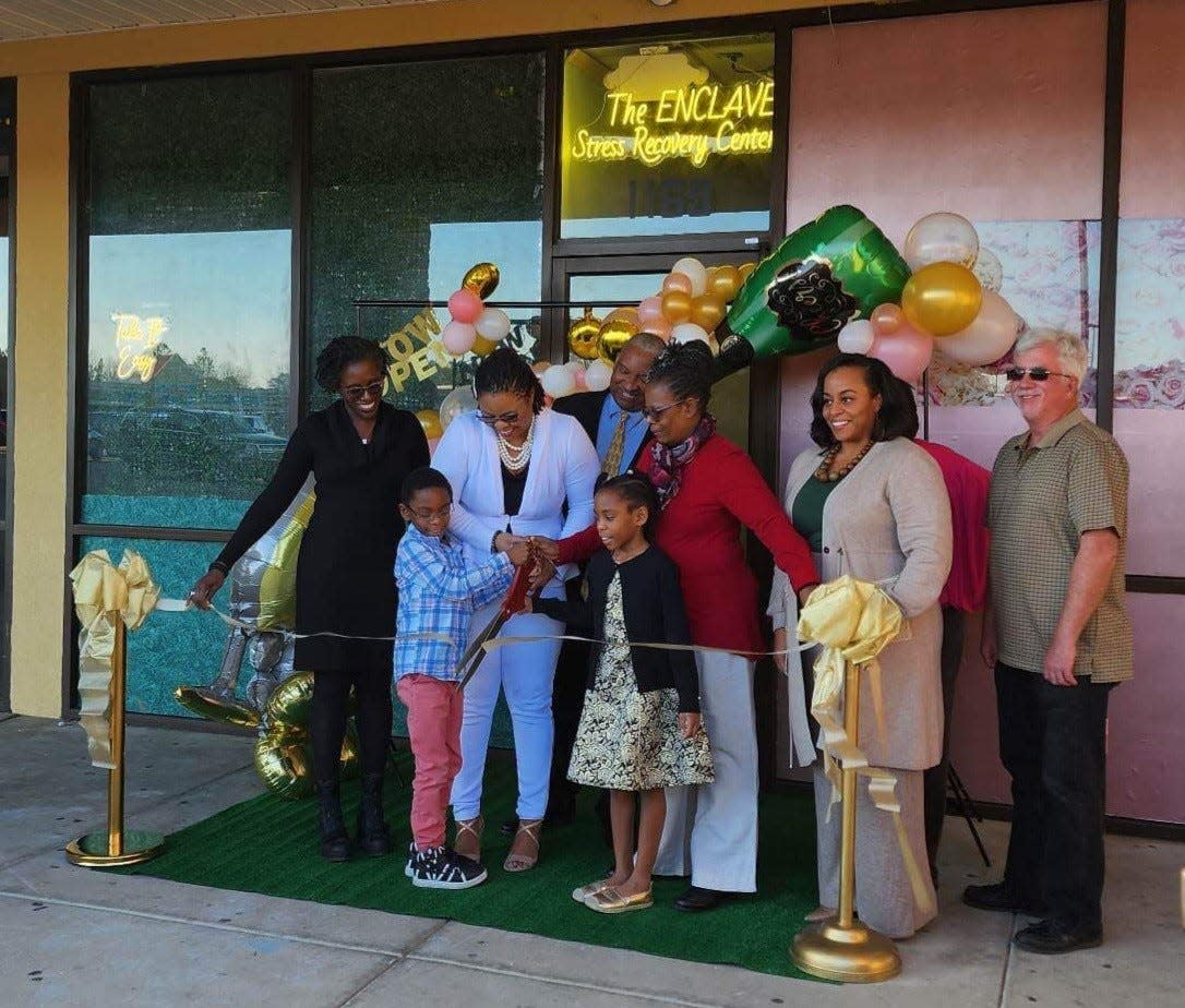 Taneshia Kerr, with scissors, cuts the ribbon for The Enclave Stress Recovery Center at Southwind Plaza in Spring Lake on Jan. 24, 2023. The center is designed to provide a peaceful and therapeutic setting for people to deal with stress. It features therapy suites — a Himalayan salt suite, an indoor garden, a beach room and an open floor for co-working and group sessions.