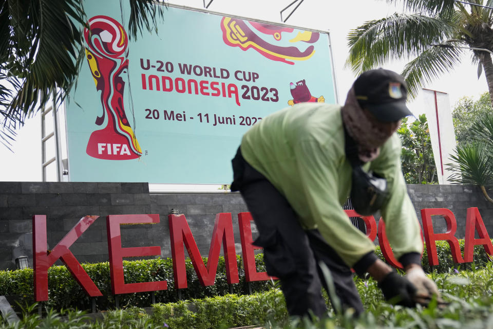 A worker trims grass near a banner of FIFA U-20 World Cup at the Ministry of Youth and Sports in Jakarta, Indonesia, Thursday, March 30, 2023. Indonesia was stripped of hosting rights for the Under-20 World Cup on Wednesday only eight weeks before the start of the tournament amid political turmoil regarding Israel's participation. (AP Photo/Dita Alangkara)
