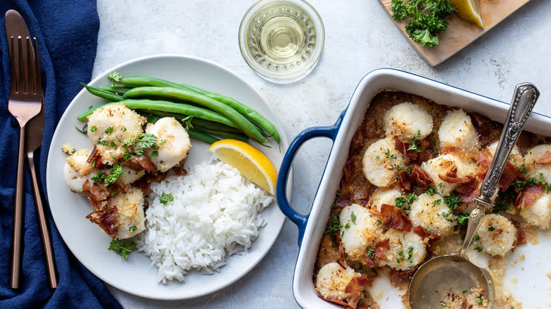 Top-down view of scallops and bacon on a plate and in a dish