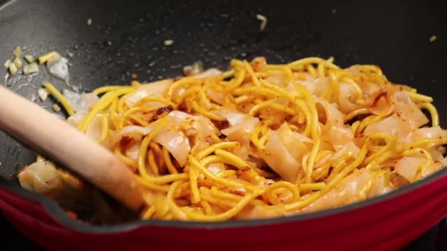 Frying yellow noodles and kway teow in a pan with wooden spatula