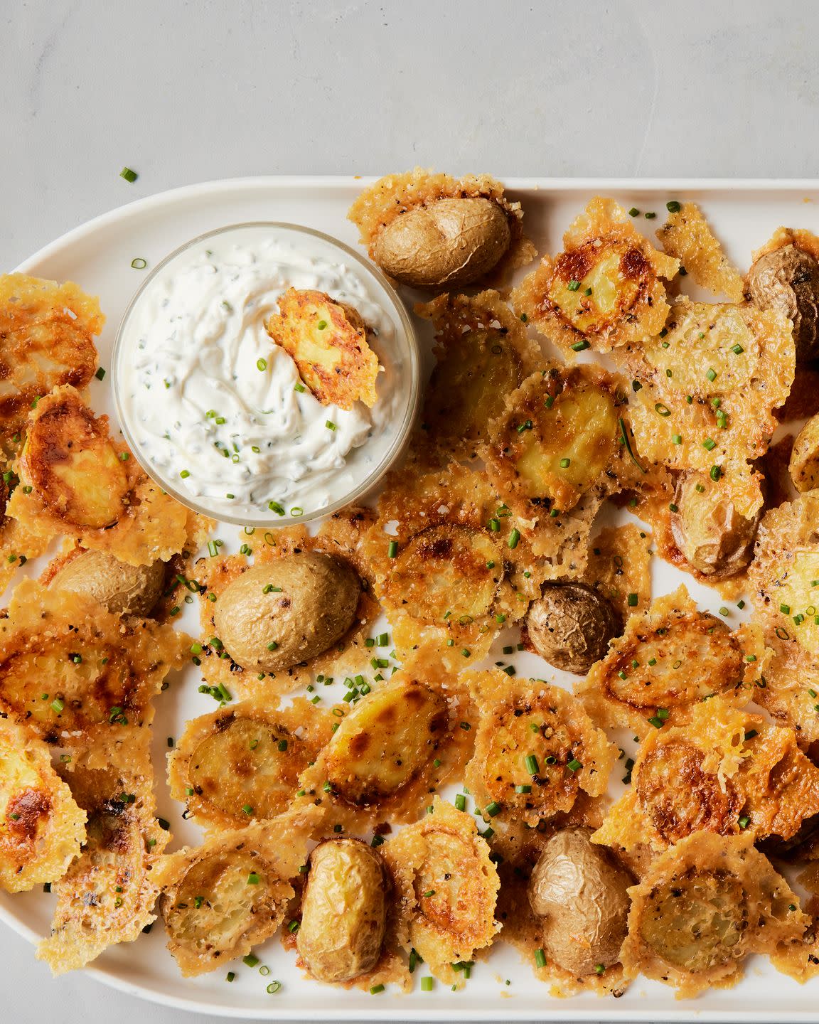 crispy parmesan potatoes on a platter with a bowl of sour cream and chive dip