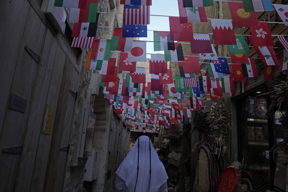 A man in Arabic attire walks through an alley at Souk Waqif decorated with the flags of countries participating in the Asian Cup, a major international soccer tournament, in Doha, Qatar, Tuesday, Jan. 16, 2024. (AP Photo/Aijaz Rahi)