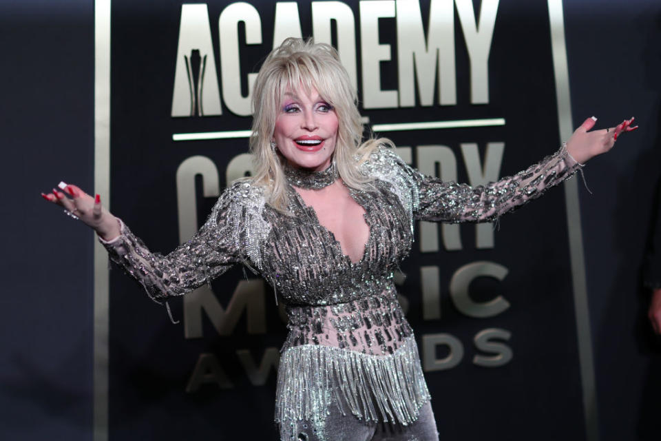 Dolly Parton poses with arms extended, wearing a sparkly outfit at the Academy of Country Music Awards