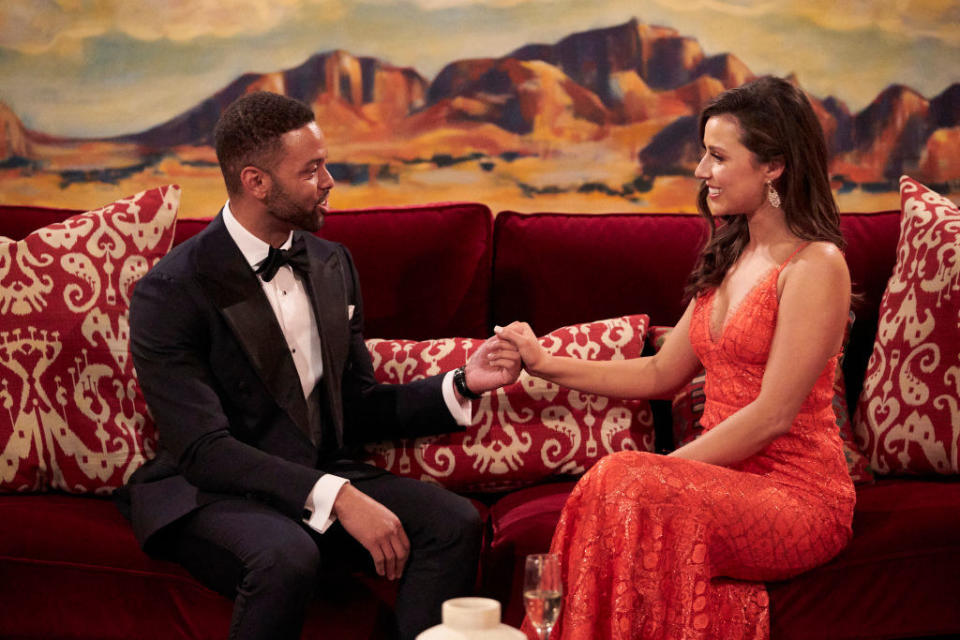 A man and a woman holding hands as they sit on a couch from an episode of The Bachelorette