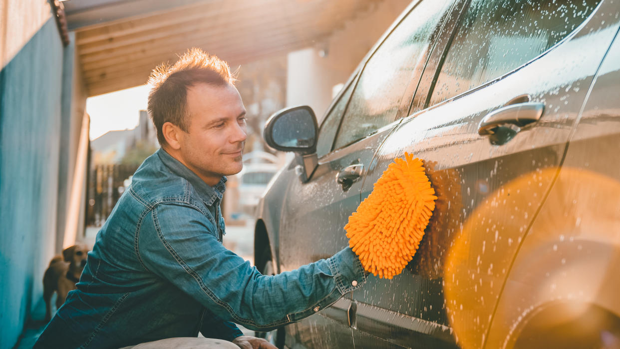 man washing his car at his house with his dog