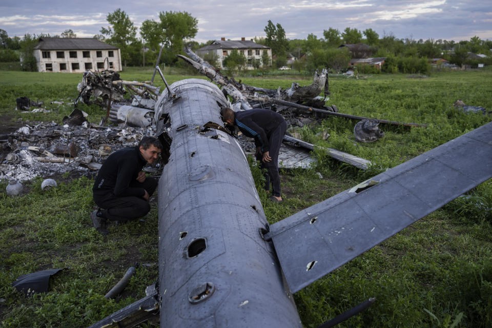Oleksiy Polyakov, a la derecha, y Roman Voitko revisan el lunes 16 de mayo de 2022 los restos de un helicóptero ruso destruido que yace en un campo en la aldea de Malaya Rohan, región de Járkiv, Ucrania. (AP Foto/Bernat Armangue)