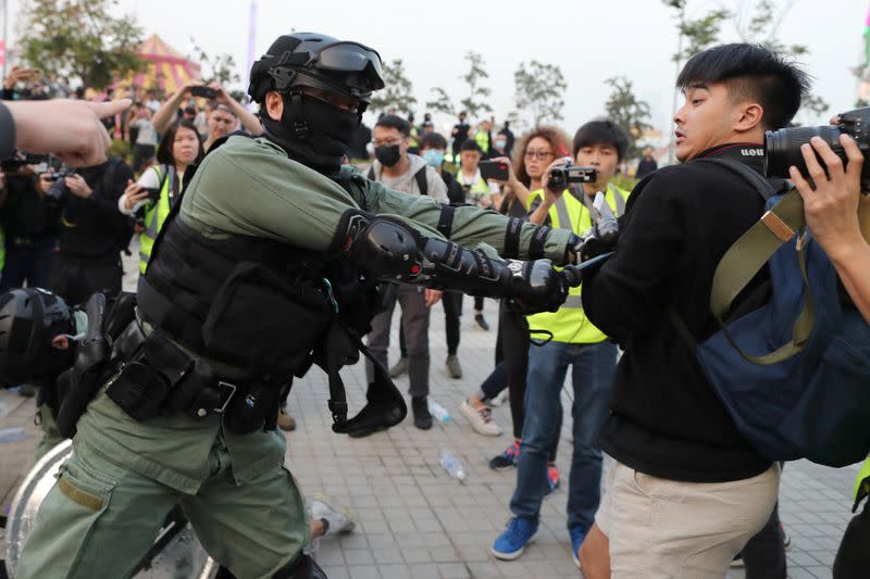 Un policía antidisturbios golpea a un hombre que sostiene una cámara mientras los manifestantes de Hong Kong se concentran en apoyo de los derechos humanos de los uigures de Xinjiang en Hong Kong