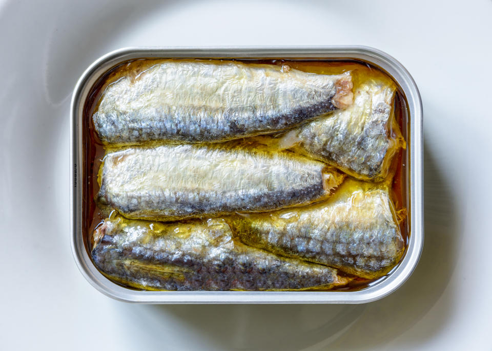 An opened can of sardines in oil on a white plate, seen from above.