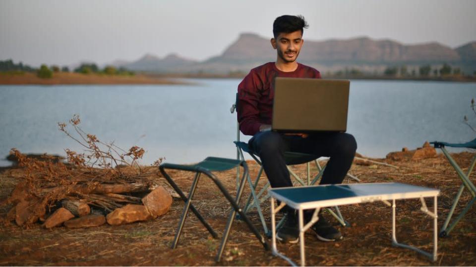 Un joven trabaja con una computadora portatil de manera remota cerca del agua.