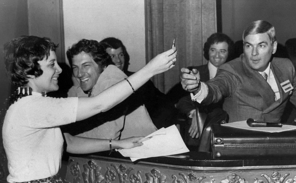 FILE - In this May 18, 1971 file photo, Evelyn Y. Davis, holds up a bullet from an ammunition bandolier she wore to a shareholders meeting of 20th Century-Fox Film Corp. in Wilmington, Del. as company official Charles M. Lewis reaches for it. Davis, commenting on the election of a new board of directors said, "Here, fight it out." For decades, Davis, who has been buying a few shares of big companies, attends their annual meetings, turning them into her personal stage. But in 2012, Davis didn't show up at any company's annual meeting. Age has finally made her do what the most powerful CEOs in America couldn't: Give it a rest. "I'm not so young anymore," said Mrs. Davis, 82. (AP Photo)