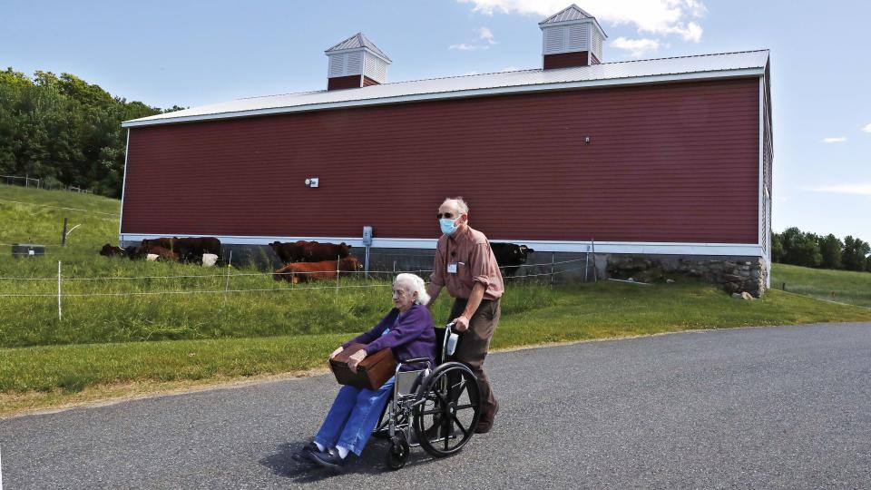 In this Monday, June 8, 2020, photo, 93-year-old Flo Young, originally from Cambridge, Mass., holds a box of pen pal letters as she takes a ride past a barn with activity aide Rich Vanderweit outside the Sullivan County Health Care nursing home in Unity, N.H. In a letter-writing effort during the virus pandemic to connect nursing home residents in two neighboring communities, residents now are receiving pen pal letters from across the United States. (AP Photo/Charles Krupa)