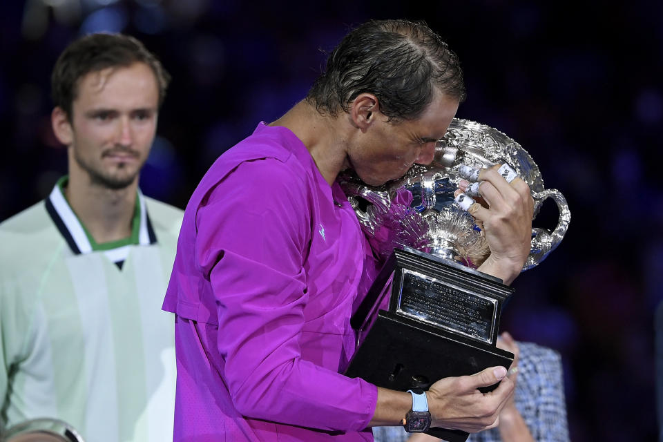 FILE - Rafael Nadal of Spain kisses the Norman Brookes Challenge Cup after defeating Daniil Medvedev, back left, of Russia in the men's singles final at the Australian Open tennis championships in Melbourne, Australia, early Monday, Jan. 31, 2022. Rafael Nadal and Novak Djokovic are both entered in the French Open, making it the first Grand Slam tournament with both of them in the field since last year’s French Open. (AP Photo/Andy Brownbill, File)