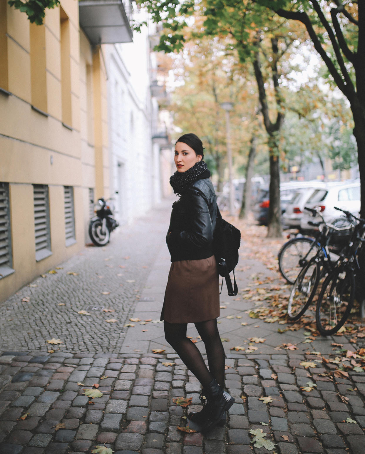 Vintage toned portrait of a young woman in Berlin, wearing a black leather jacket and a beige skirt, walking on the streets of Prenzlauer Berg, near Mitte in the late Autumn day. Street style, casual fashion concept.