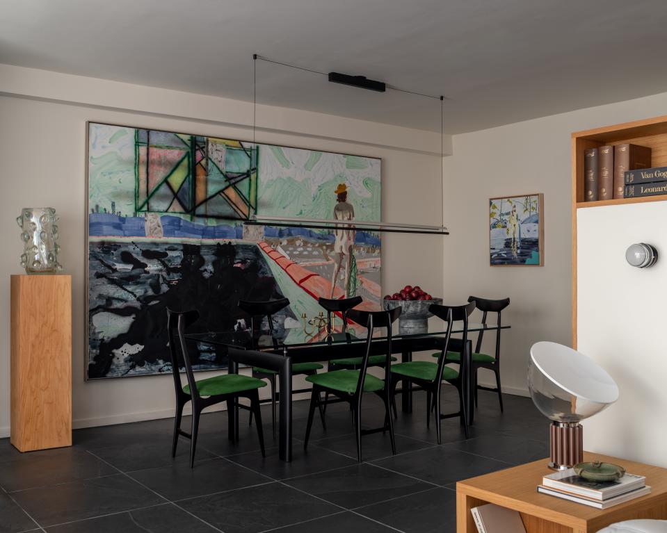 The dining room is an emerald oasis composed of an LC6 glass table by Le Corbusier, Pierre Jeanneret and Charlotte Perriand, and restored midcentury Italian chairs. Large-scale and small-scale paintings by Skyler Brickley envelop the space. The pendant is by Santa & Cole.